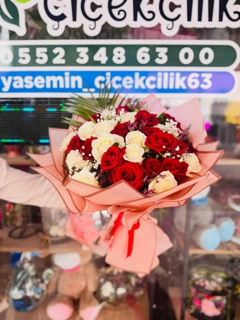 Pembe ambalaj içinde kırmızı ve krem-beyaz güller; işletmenin tabelası önünde.