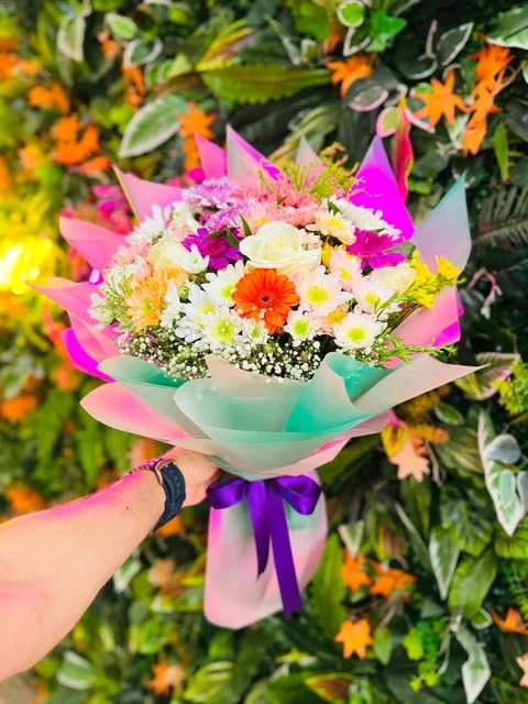 Beyaz güller, beyaz papatya görünümlü çiçekler ve turuncu gerbera; mint-pembe ambalaj, mor kurdele.